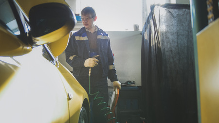 Car mechanic male blows air filter of automobile in service