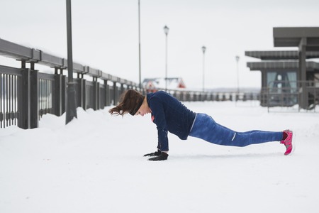 Sport girl model doing pushups during work out fitness at snow winter outdoor