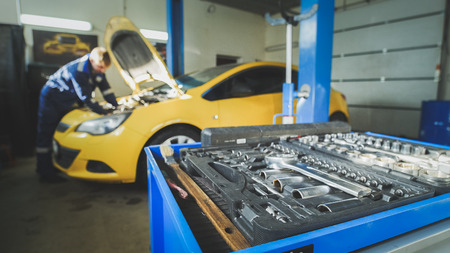 Defocused - a worker mechanic checks the electrical in the hood of the yellow car, garage workshopの写真素材