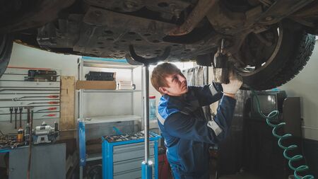 Mechanic unscrewing parts of automobiles bottom under lifted carの写真素材