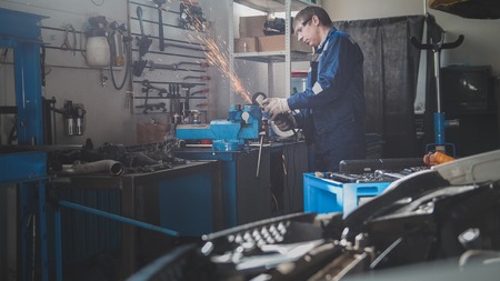 Car auto workshop - male caucasian mechanic worker works with circular saw
