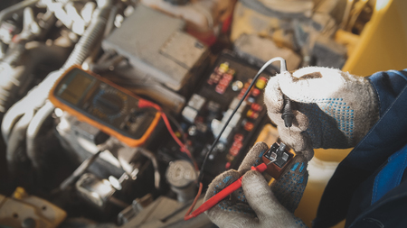 Mechanic works with car electrics - electrical wiring, voltmeter