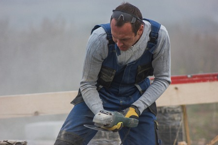 Worker man builder working with circular saw outdoors, sawdust flying around