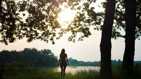 Beautiful Young Woman near forest lake at sunrise or dusk, silhouetteの写真素材