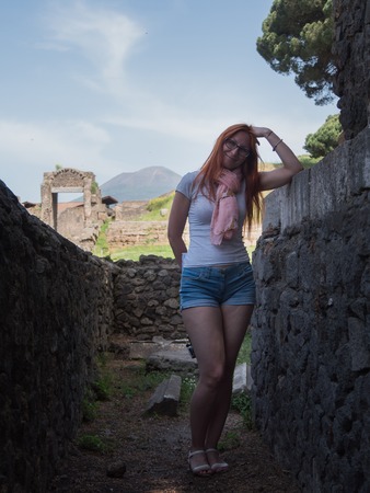 Beautiful red hair woman in glasses and shorts standing in pompeii, Italy - hot summer middayの写真素材