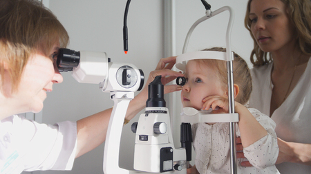Doctor optometrist checks little girls eyesight - mother and child in ophthalmologist roomの写真素材