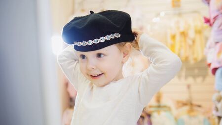 Childs dress store - little blonde baby girl doing shopping and buying pretty hatの写真素材