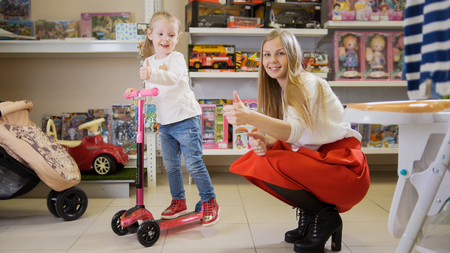 Happy little girl with mommy playing with bicycle in kids storeの写真素材