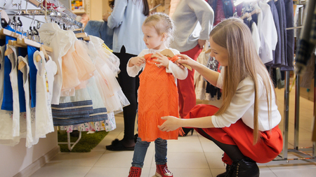 Cute little girl with mommy buying red dress in store of kids clothesの写真素材