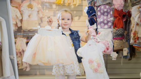 Shopping for girls - blonde little girl showing new purchases in store of childs clothesの写真素材