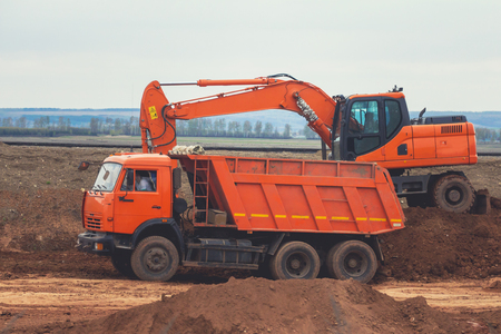 Red wxcavator loading dumper truck at construction of the roadの写真素材