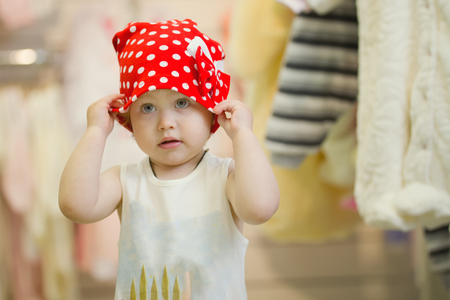Little cute 3 years girl in a red hat polka dot at children clothes storeの写真素材