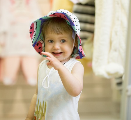 Cute girl tries on colourful hat in children storeの写真素材