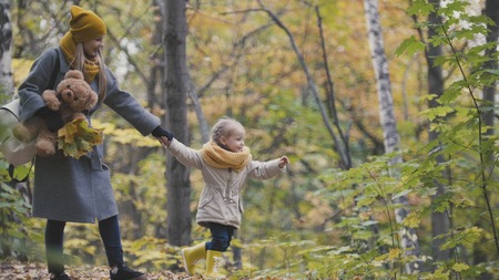 Little daughter with her mommy and Taddy bear walks in autumn park - plays the leavesの写真素材