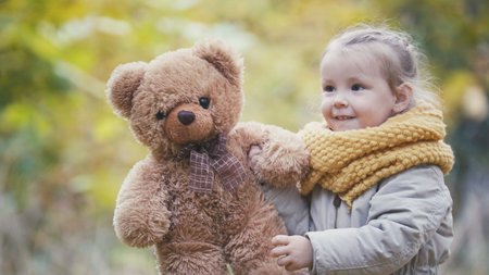 Little blonde girl plays with teddy bear in autumn parkの写真素材
