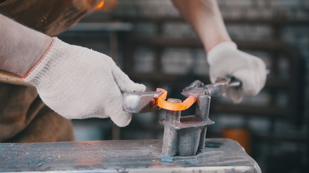 Close up view - hands of Blacksmith with gloves in forge makes steel knifeの写真素材