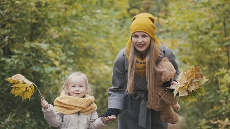 Blonde girl with her mommy in autumn park - play and clap handsの写真素材