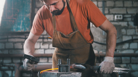 The smith gives shape with a hammer to a red-hot metal object