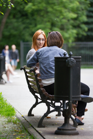 A girl in glasses sits on a bench next to a girlfriendの写真素材