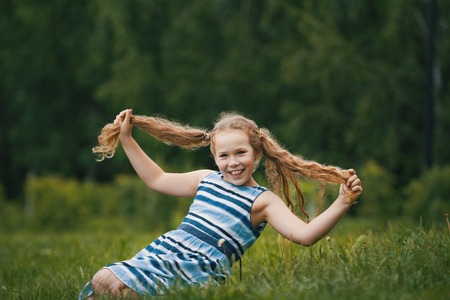 Smiling child girl wearing blue summer dress is playing in parkの写真素材