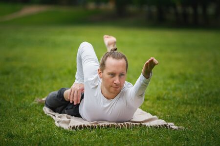 Hipster man - yoga instructor performs flexibility exercises in park