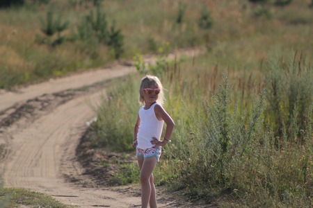Cute little child girl in sunglasses standing on summer dusty rural roadの写真素材