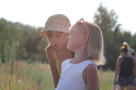 Two little sisters walking in a summer meadow at sunny day