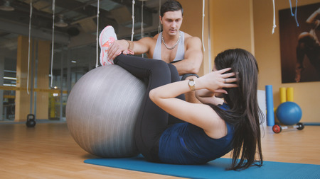 Girl doing workout for abs with fit-ball and muscular instructor