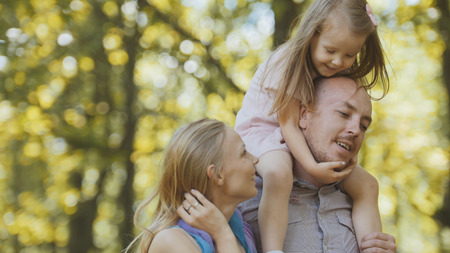 Father, mother and daughter having fun in park at sunny dayの写真素材