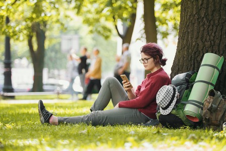 Girl teenager tourist with backpack looking at smartphone in city parkの写真素材