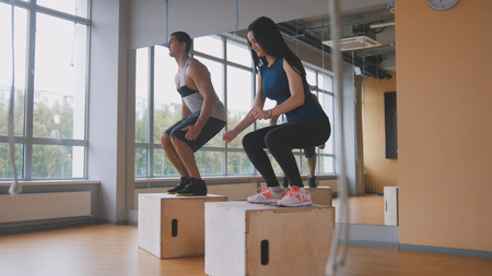 Sportive young woman and muscular man fitness instructor doing box jump exercise during a workout at the gymの写真素材