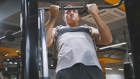 Bodybuilder in the gym performs pull up for biceps with metal chainの写真素材