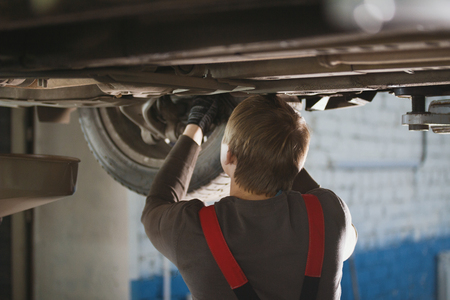 Mechanic unscrewing parts of automobiles bottom under lifted carの写真素材