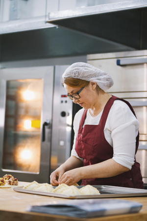 Adult woman in glasses and apron bakes cakes in the bakeryの写真素材