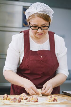 Adult woman in glasses and apron bakes cakes in the bakery face