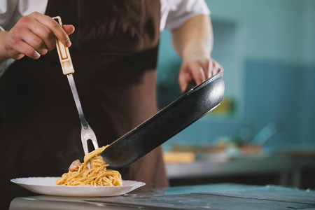 Chef serves spaghetti carbonara on the plate in restauranteの写真素材
