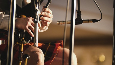 Bagpipe player in a kilt plays musical instrument at the stage