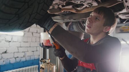 Mechanic with the lamp is checking the bottom of car in garage automobile service, close upの写真素材