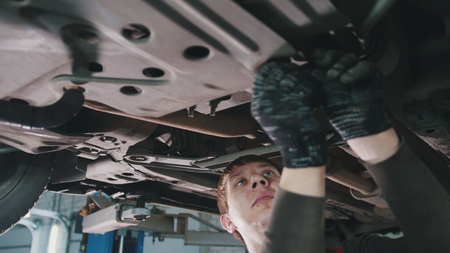 Car service workshop - mechanic unscrews detail of car under bottom of vehicleの写真素材