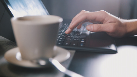 Man drinking coffee and use laptop in cafe - close up