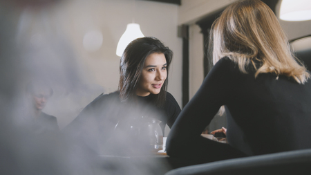 Black haired young woman with black hair drinking coffee and talking with girlfriend in the cafeの写真素材