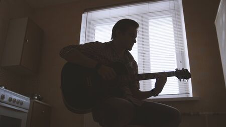 Young attractive musician composes music on the guitar and plays, other musical instrument in the foreground, silhouetteの写真素材
