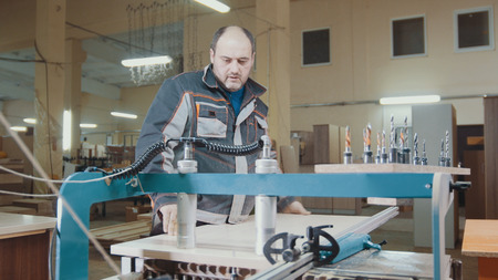 Worker carpenter cut a wooden workpiece on a furniture factory