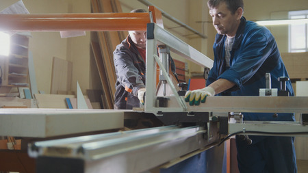 Workers at factory are cutting wooden fragment on electric saw at furniture industryの写真素材