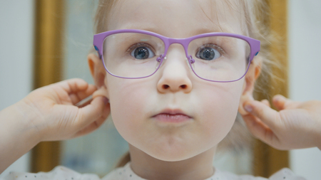Little girl tries fashion medical glasses near mirror - shopping in ophthalmology clinicの写真素材