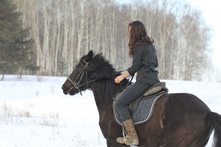 Young black hair woman with a horse in winter snowy forest
