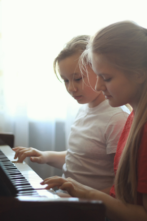 Two teenagers sisters girl 14-years old plays the piano at home, vertical shotの写真素材