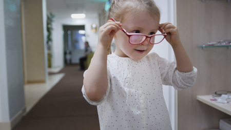Little girl tries fashion medical glasses near mirror - shopping in ophthalmology clinicの写真素材