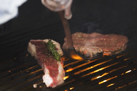 Preparing meat on the grill, chef flips the piece with shovelの写真素材