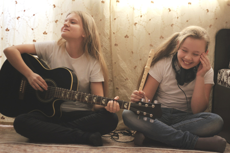 Two female teens playing musical instruments, guitar and flute, at homeの写真素材